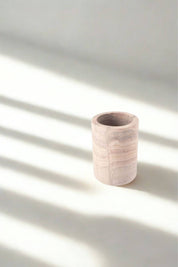 Minimalist rainbow sandstone tumbler with soft blush and taupe striations, photographed in natural light with striped shadows.