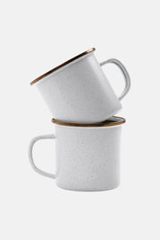 Two handcrafted white speckled enamel cups against white background