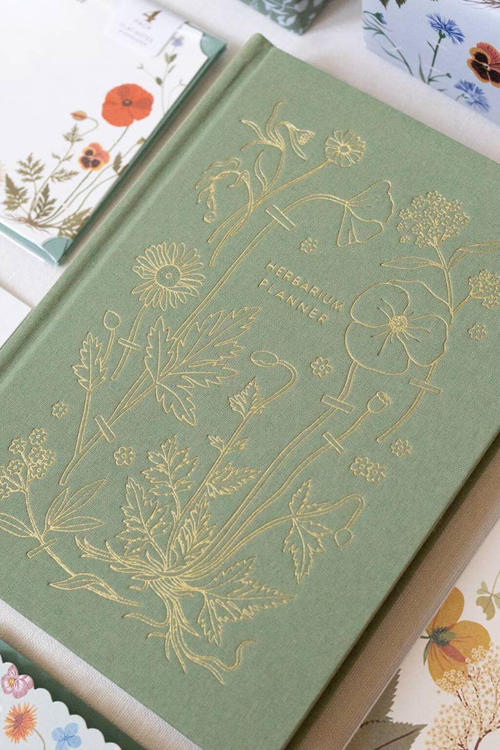 Linen-bound sage green Herbarium planner with gold foil botanical embossing.