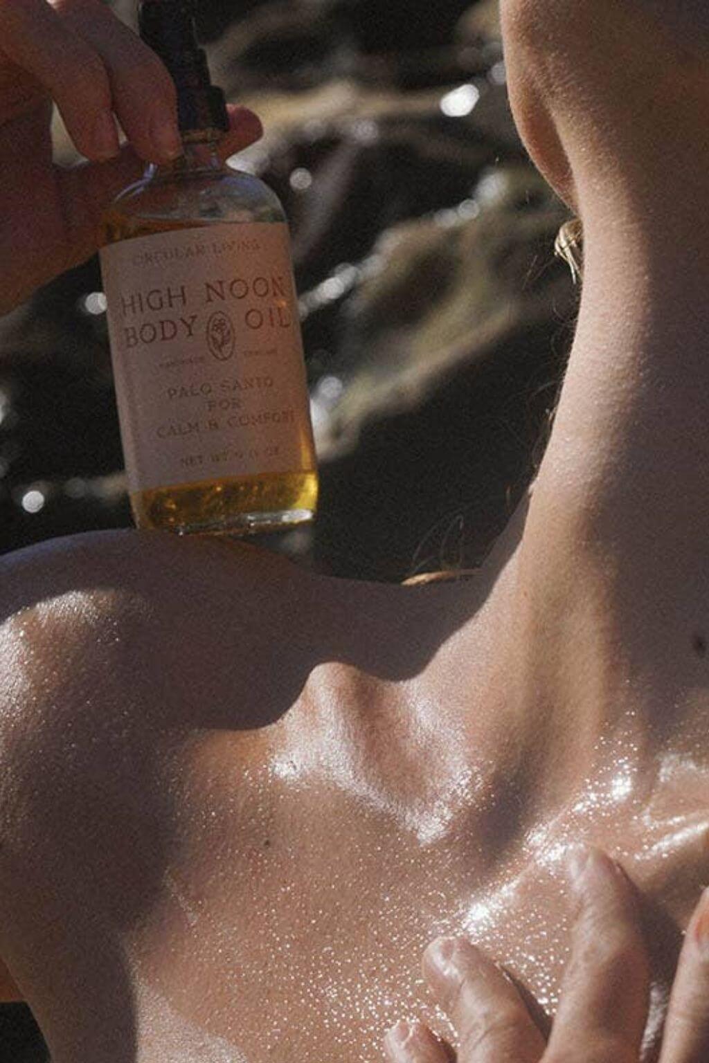 Applying High Noon Body Oil to sunlit shoulder, glowing skin