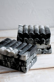 Two stacks of Ridge Black Marble Soap Dishes with natural veining, placed side by side on a light wooden table.