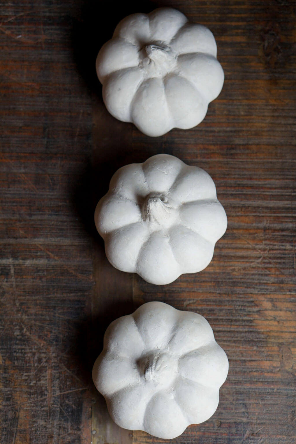 Three white paper mache pumpkins on a wooden surface