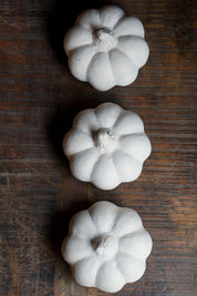Three white paper mache pumpkins on a wooden surface