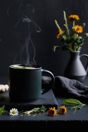 Steaming cup of Lunar Logic Constellations Within Gut Restoration Tea with fresh chamomile, calendula, and mint