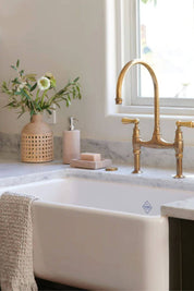 armhouse kitchen sink vignette with brass faucet, marble countertop, and the Rainbow Sandstone Soap Dispenser alongside a natural rattan vase and bar soap.