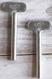 Two silver Metal Tube Roller Keys laid flat on a wooden surface, embossed with a dove motif and the words "Pré de Provence."