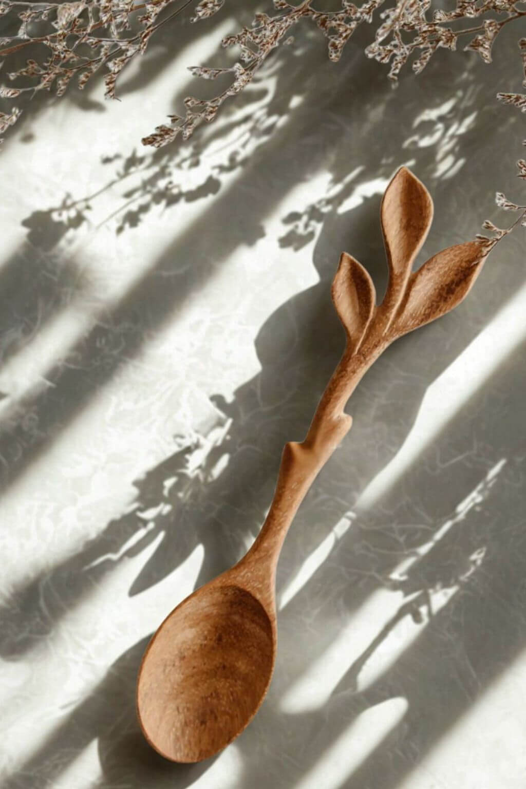 Leaf Cluster Doussie Wood Spoon resting on textured linen surface.
