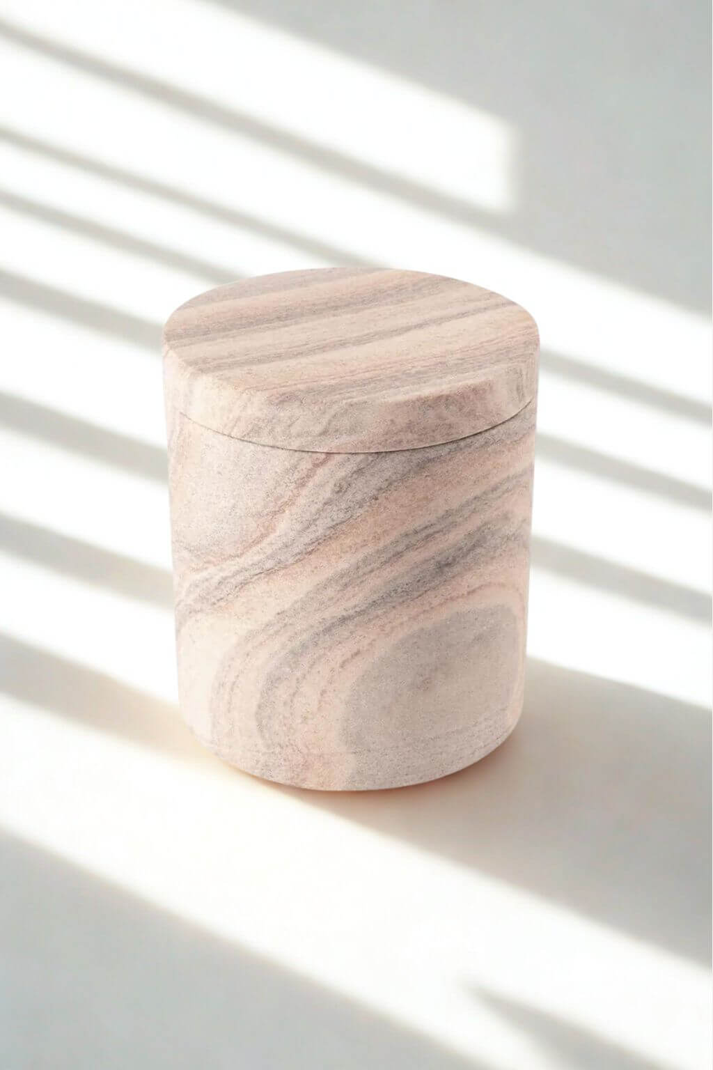 Close-up of rainbow sandstone jar with lid, featuring swirling blush, taupe, and cream striations in the natural stone.