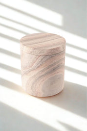Close-up of rainbow sandstone jar with lid, featuring swirling blush, taupe, and cream striations in the natural stone.