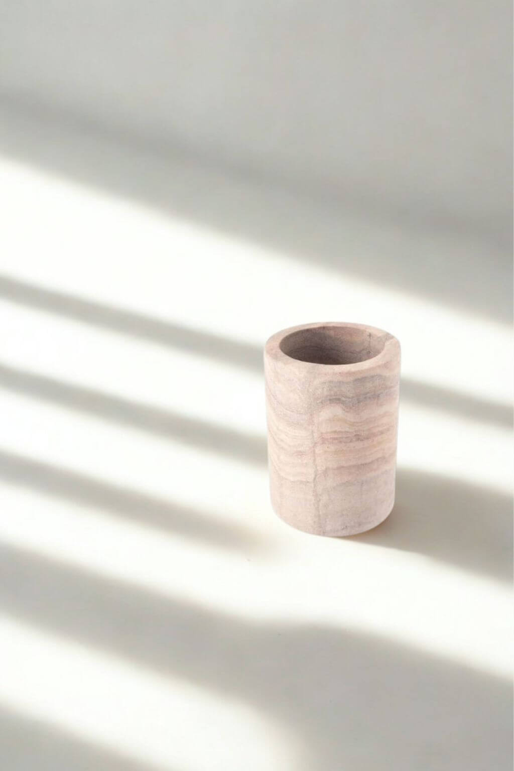 Minimalist rainbow sandstone tumbler with soft blush and taupe striations, photographed in natural light with striped shadows.