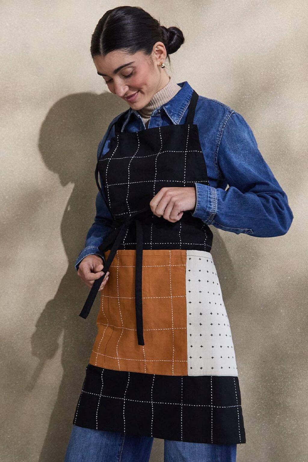 Person wearing a patchwork apron with a blue shirt and jeans against a beige background