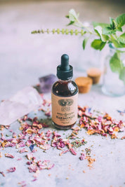 A bottle of Anima Mundi Harmonize Tonic with rose petals and crystals in the background