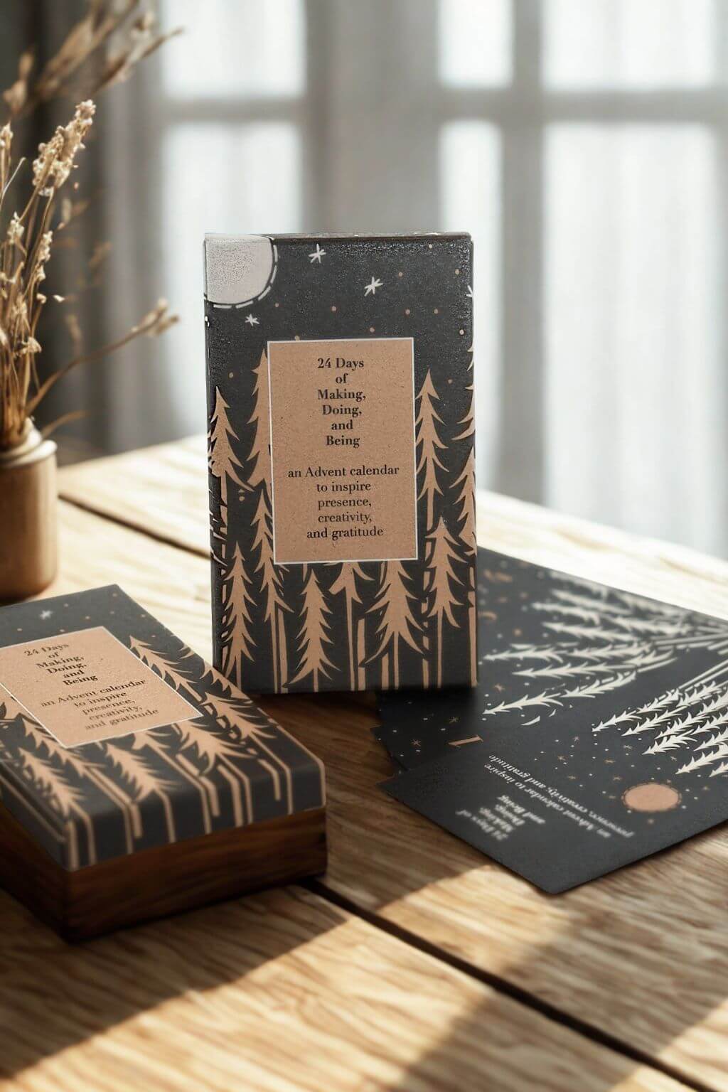 Advent calendar box with moonlit forest design printed in gold on black paper, resting on a wooden table in soft winter light.
