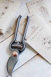 Pruner on a wooden surface with botanical-themed cards in the background