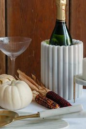 Waterloo marble bottle holder displayed with champagne, pumpkins, and brass serving utensils on a harvest table.