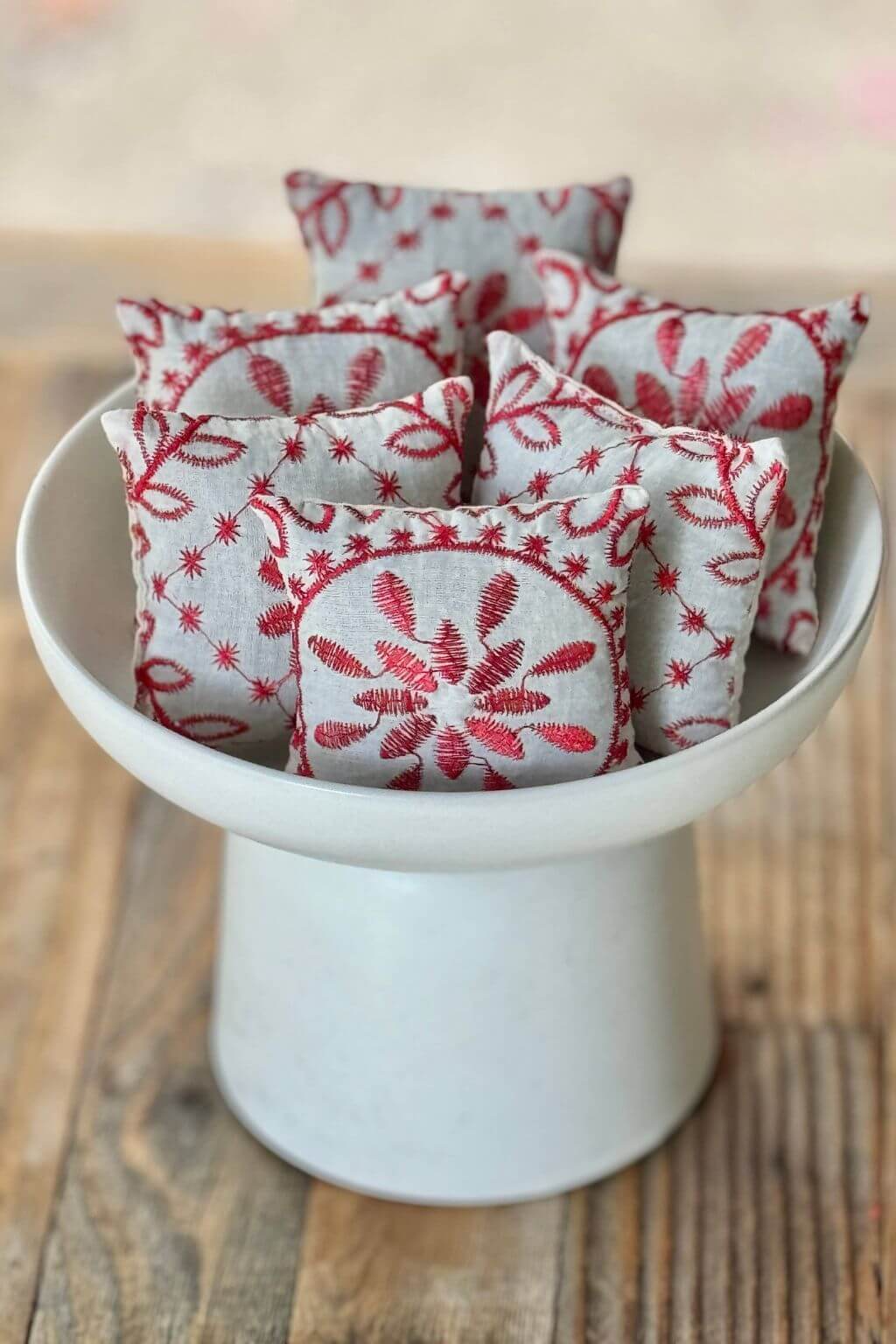 Scandinavian embroidered lavender sachets in red and white linen, displayed in ceramic bowl.
