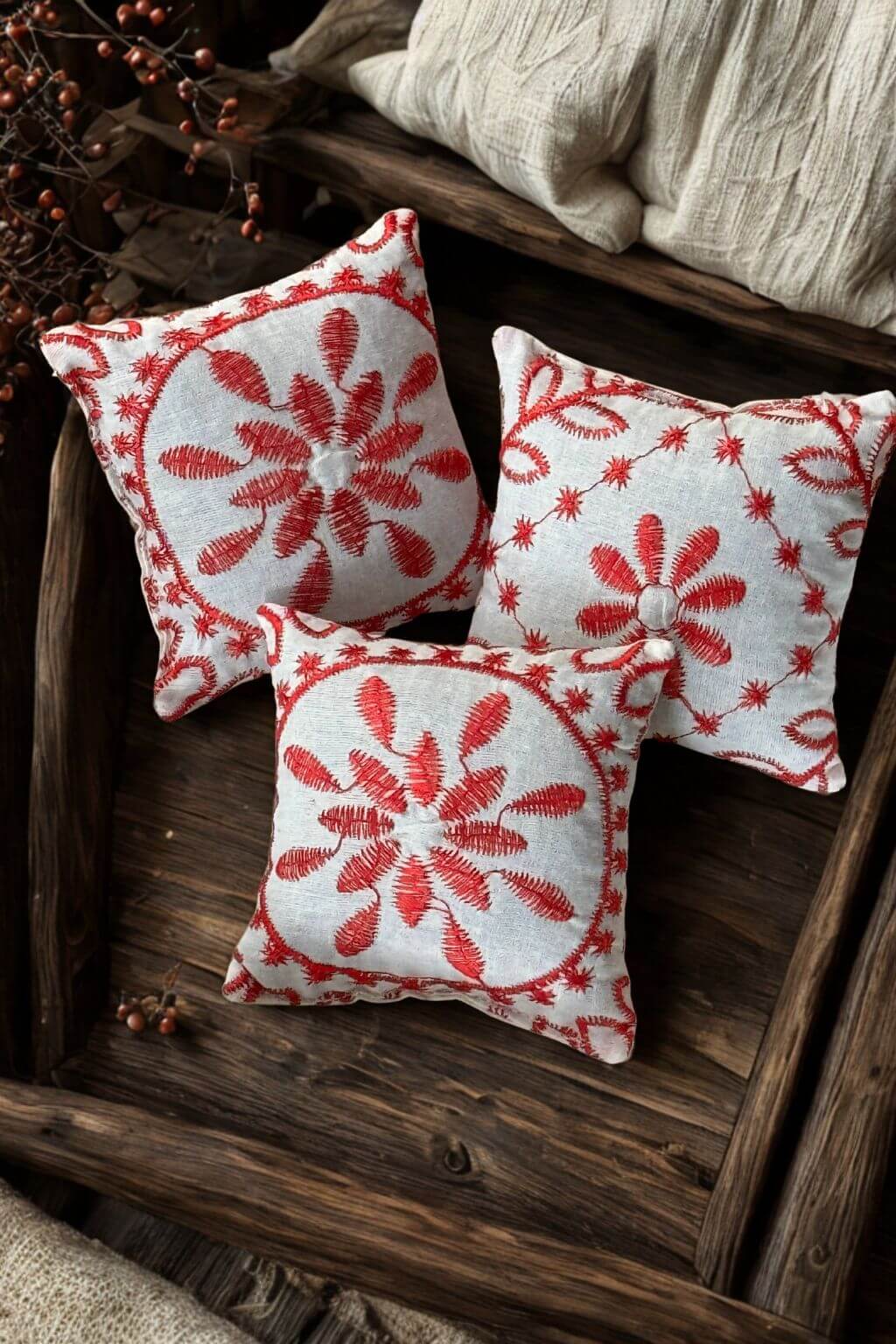 Handcrafted set of three red embroidered lavender sachets resting on rustic wood tray.