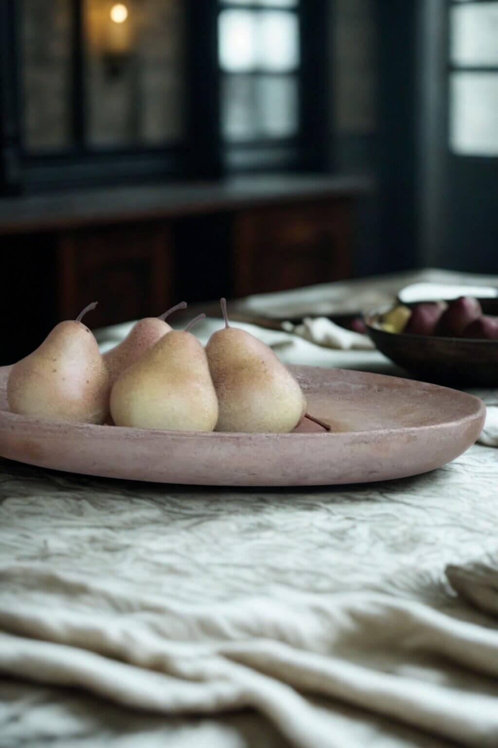 Round travertine tray styled with pears in natural light on a rustic linen tablecloth.