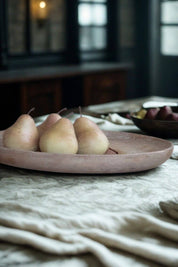 Round travertine tray styled with pears in natural light on a rustic linen tablecloth.