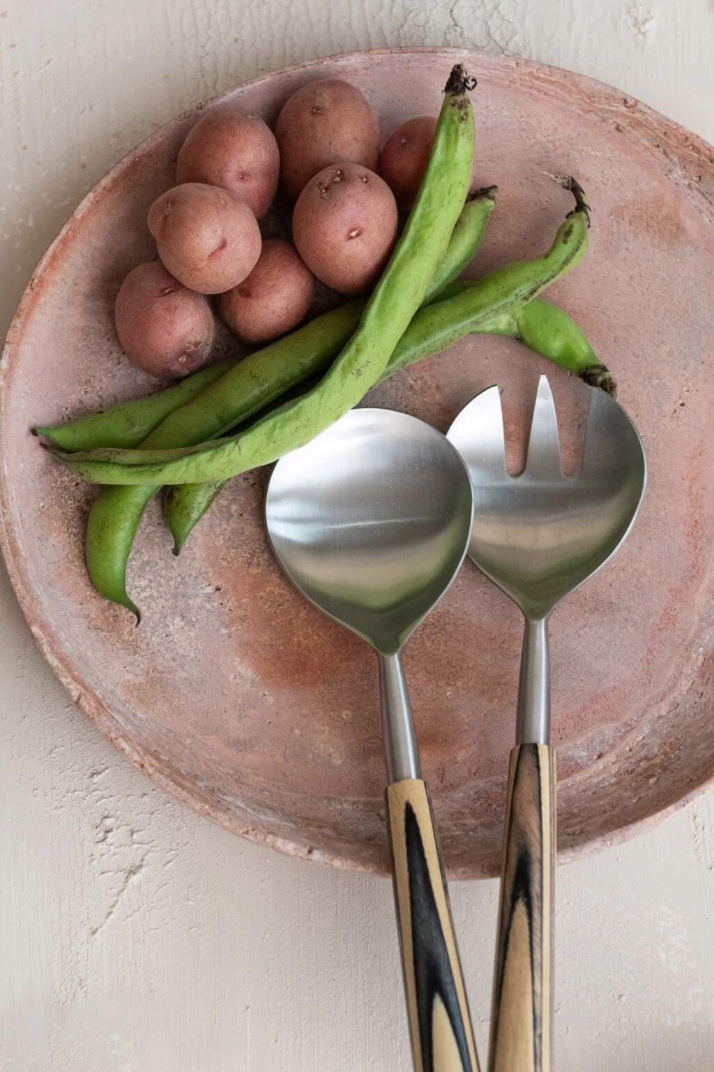 Handcrafted red travertine tray with potatoes and green beans on neutral linen table.