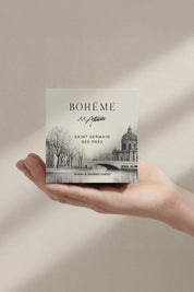 Hand holding Bohème Saint-Germain-des-Prés candle box, featuring Parisian architecture illustration