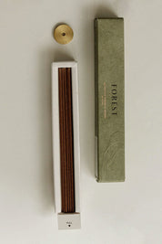 Open box of "Forest" Japanese incense sticks lying flat beside a brass incense holder, highlighting the neat arrangement of sticks inside the package.
