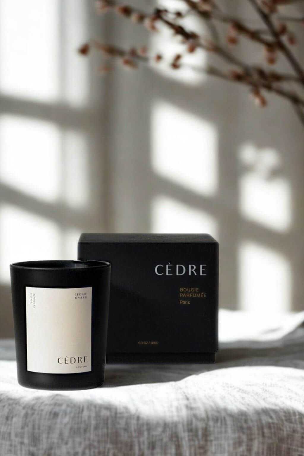 Minimalist black Cedar Luxury Candle and box, styled with soft-focus branches in a serene interior.