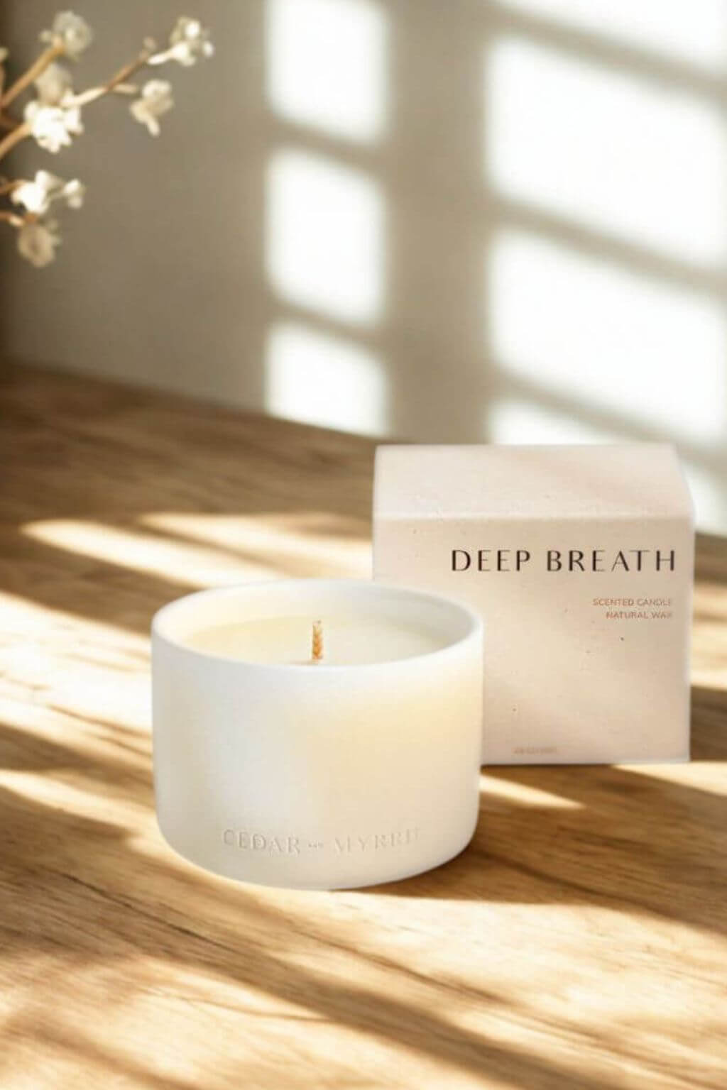 Deep Breath candle and box on a wooden surface with sunlight streaming through window shadows.