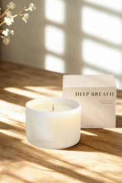 Deep Breath candle and box on a wooden surface with sunlight streaming through window shadows.
