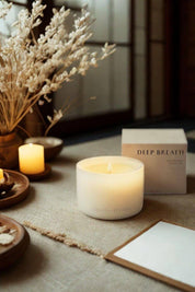 Lit Deep Breath candle surrounded by natural decor, with packaging in the background and warm ambient lighting.