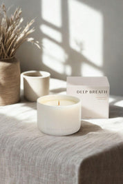 White ceramic Deep Breath candle by Cedar & Myrrh on a linen-draped table with box packaging in the background, styled with dried botanicals.