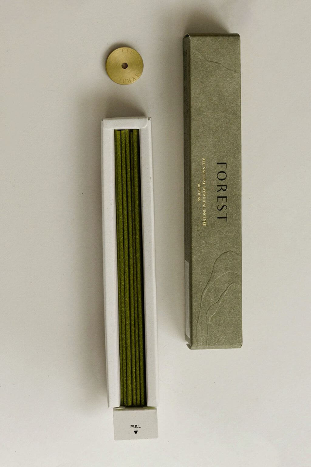 Open box of Hinoki Japanese incense sticks laid flat, revealing neatly arranged green incense sticks alongside the packaging and brass holder.