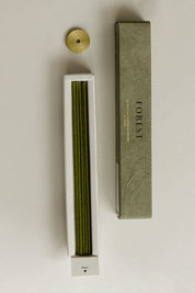 Open box of Hinoki Japanese incense sticks laid flat, revealing neatly arranged green incense sticks alongside the packaging and brass holder.