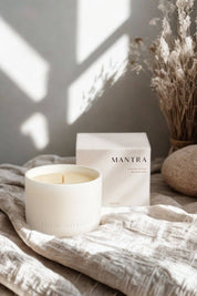 Mantra Wellness Ritual Candle styled on soft linen fabric beside dried botanicals, paired with its cream packaging in natural sunlight.