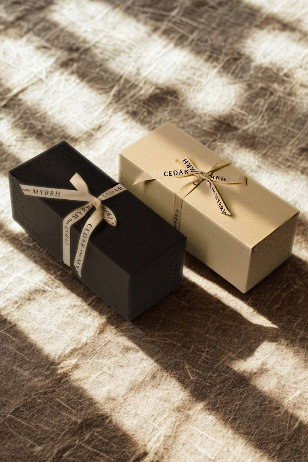 Black and cream gift boxes tied with Cedar & Myrrh ribbons, bathed in natural sunlight on a textured linen surface.