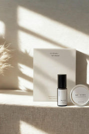 Cedar + Myrrh roller bottle of Bonne Nuit, and Me Time Balm with embossed gift box on a textured surface with sunlight casting shadows