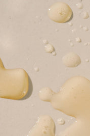 Golden drops of High Noon Body Oil on neutral background
