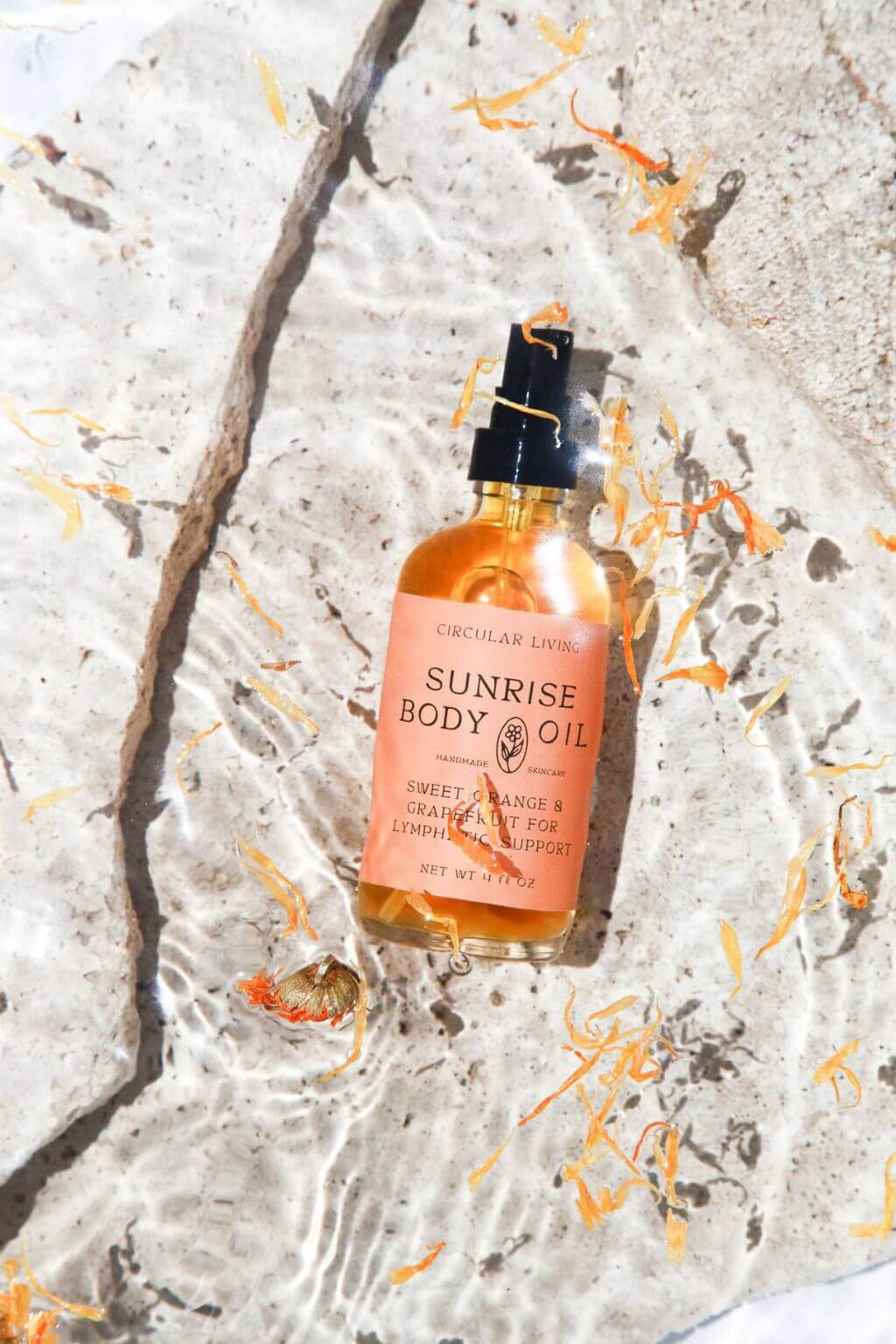 Sunrise Body Oil floating in clear water with calendula petals.