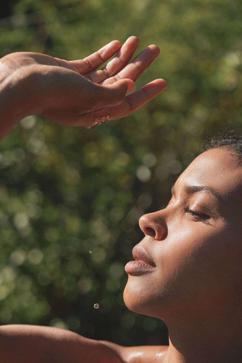Woman’s serene profile bathed in golden evening light with droplets in the air.