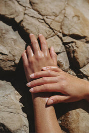 Hands glistening with body oil resting on natural stone outdoors.