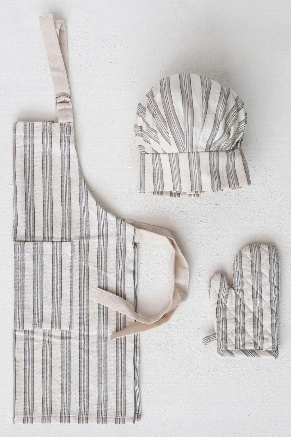Child-sized striped apron, chef hat, and oven mitt set arranged on white background