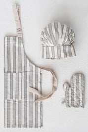 Child-sized striped apron, chef hat, and oven mitt set arranged on white background