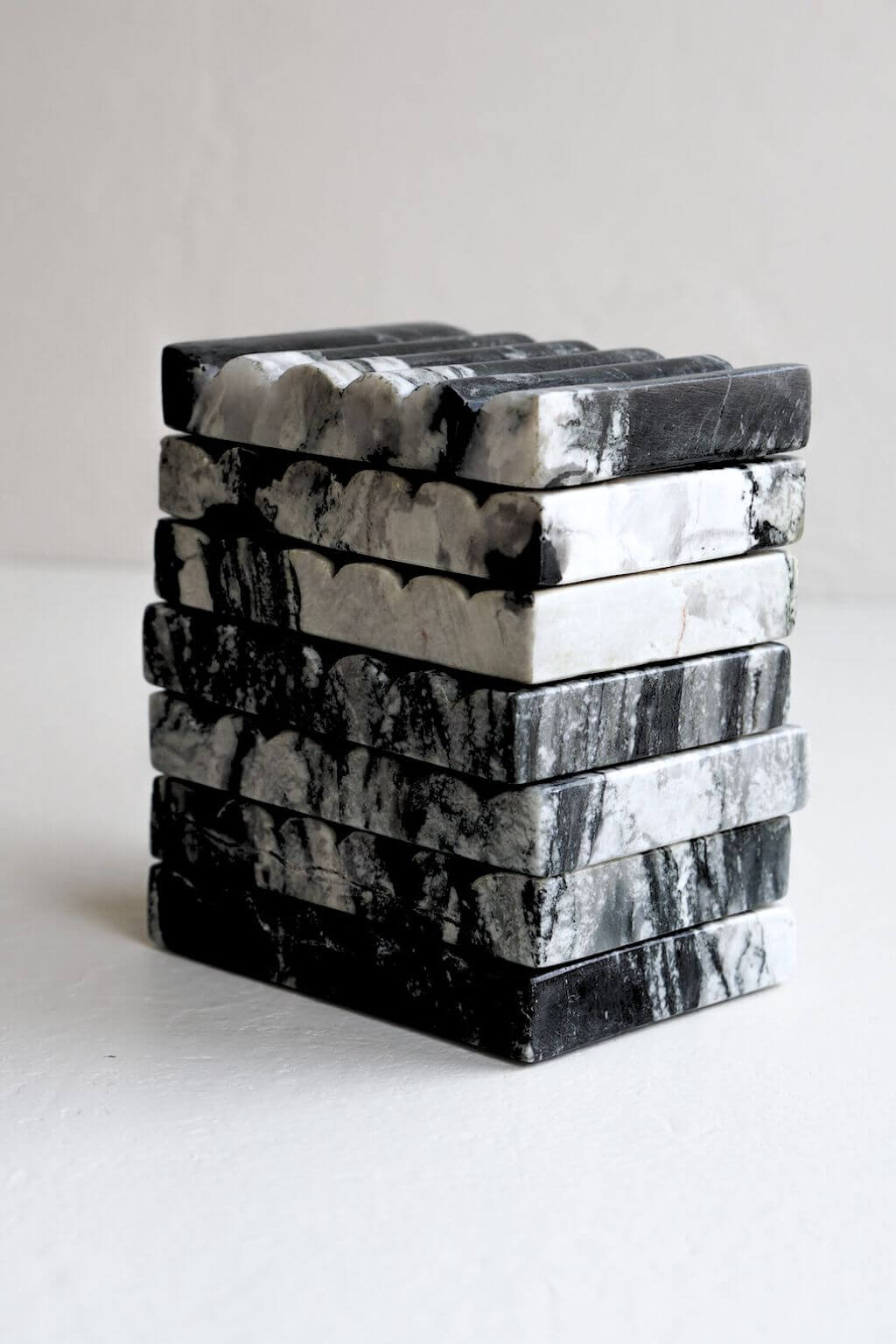 Stack of hand-carved black marble soap dishes with natural gray and white veining, displayed on a white surface.