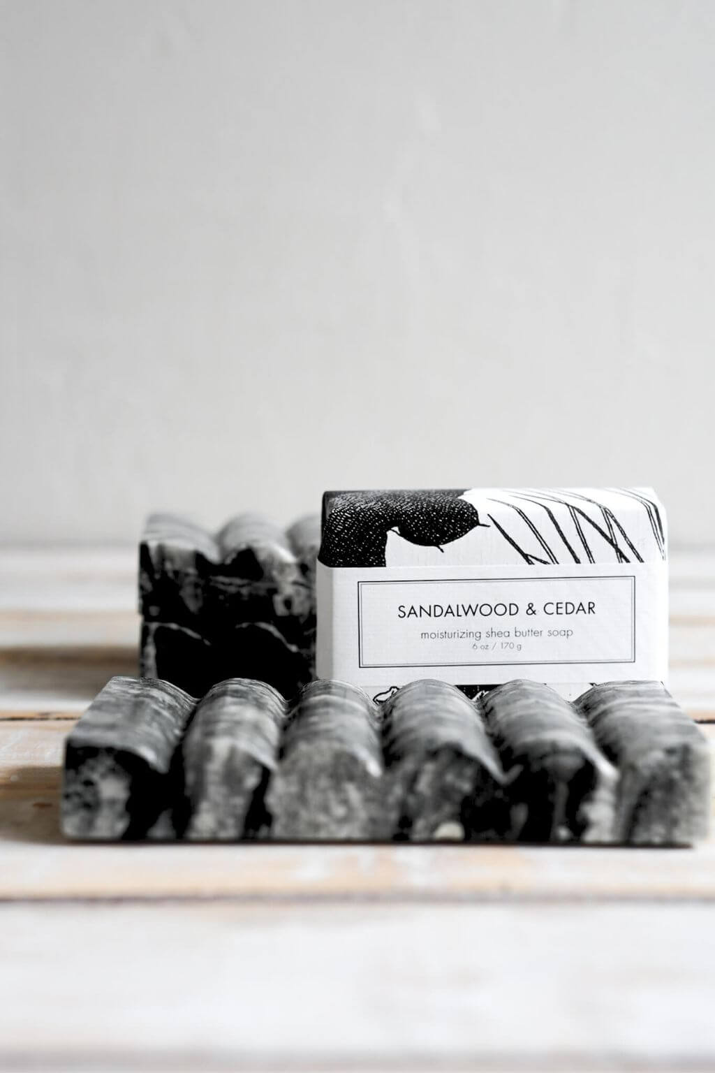 Black marble soap dish holding a Sandalwood & Cedar bar soap on a rustic wooden surface.
