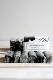 Black marble soap dish holding a Sandalwood & Cedar bar soap on a rustic wooden surface.