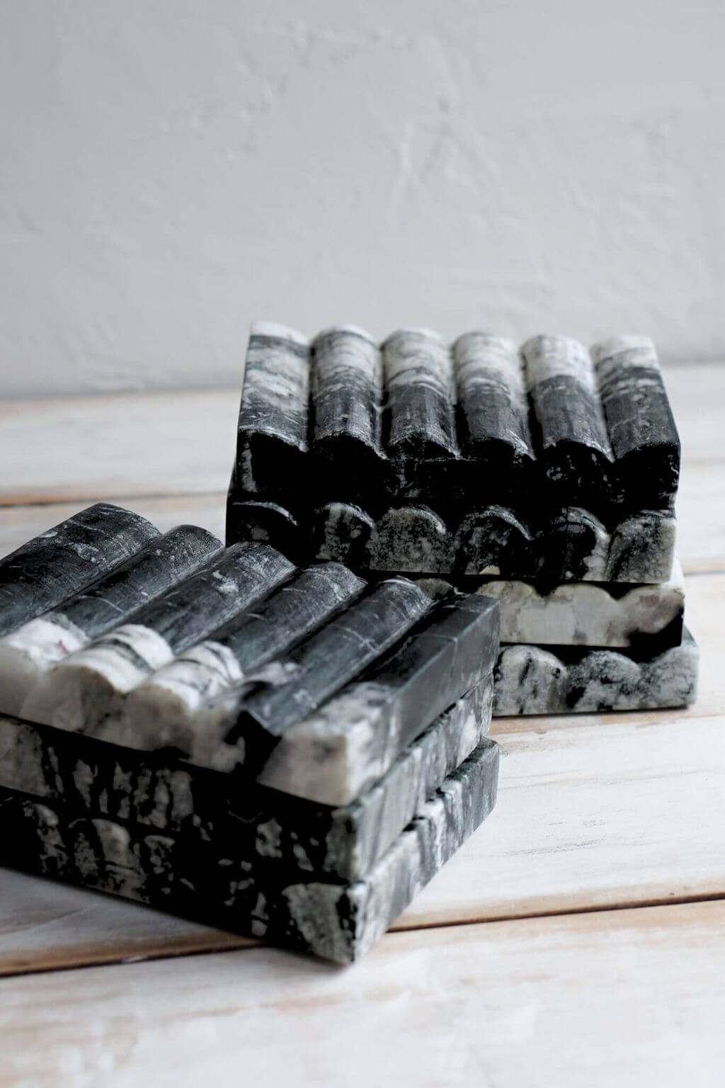 Two stacks of Ridge Black Marble Soap Dishes with natural veining, placed side by side on a light wooden table.