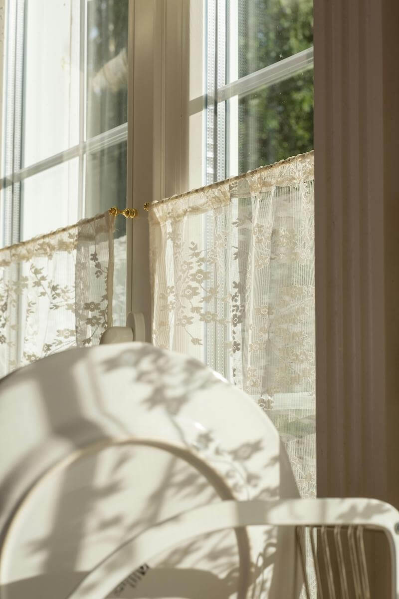 view of trees from a inside a kitchen with vintage lace curtains