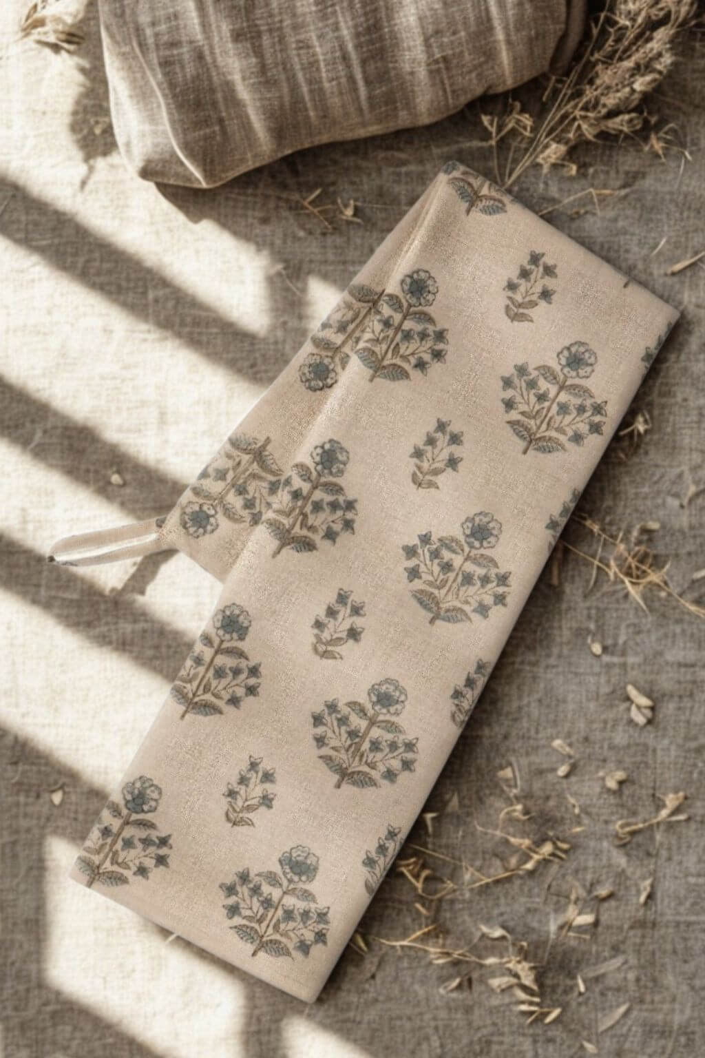 Folded Salvia Dish Towel with hand-blocked floral pattern on a textured surface with dried grass and linen