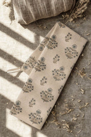 Folded Salvia Dish Towel with hand-blocked floral pattern on a textured surface with dried grass and linen