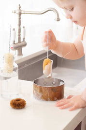 Child using small dish brushes at a kitchen sink